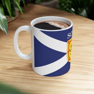 May include: White ceramic coffee mug with a blue and white Scottish flag design. The mug has a black coffee inside and the text "Scotland" is printed on the side.