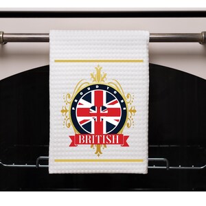 May include: White kitchen towel with a gold design featuring the Union Jack flag and the text "Proud to be British".