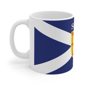 May include: White ceramic mug with a blue and white Scottish flag design. The flag features a white diagonal cross on a blue background with a yellow and red Scottish coat of arms in the upper right corner.