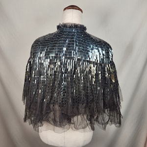 May include: A black sequined cape with a ruffled trim. The cape is made of a sheer fabric and has a high neckline.