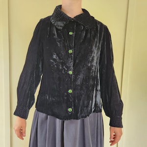 May include: A black velvet blouse with a ruffled collar and green button accents.