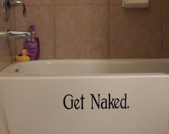 May include: A white bathtub with the words "Get Naked." written on the front. The bathtub is in a bathroom with beige tile walls.