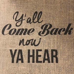 May include: A burlap sign with the text "Y'all Come Back Now YA HEAR" in black lettering.