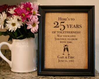 May include: A framed burlap print with black text that reads "Here's to 25 years of togetherness! May your love continue to grow with time. Gail & Eric June 14, 1993".