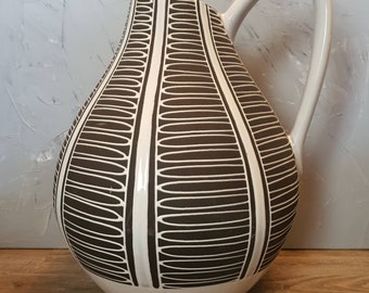 May include: A white ceramic pitcher with a brown geometric pattern. The pitcher has a wide base and a narrow neck with a curved handle.