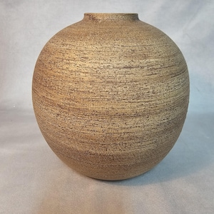 May include: A round, textured vase with a narrow neck. The vase has a warm, earthy color with horizontal lines across the surface. The vase is a decorative item.