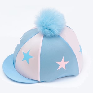 K&ouml;nnte beinhalten: Hellblauer und wei&szlig;er Reithelm mit Sternen und einem hellblauen Bommel. Der Helm hat einen gebogenen Schirm und ist f&uuml;r den Reitsport konzipiert.