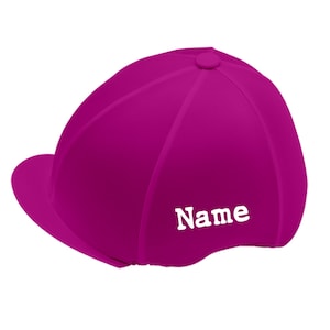 Può includere: Casco da equitazione magenta con una piccola visiera e una parte superiore arrotondata. La parola "Name" è stampata in bianco sul lato. Questo casco è progettato per la sicurezza e la protezione durante l'equitazione.