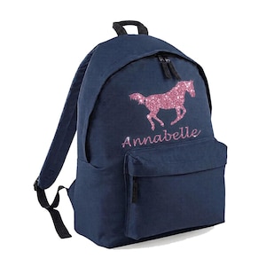 May include: A navy blue backpack featuring a pink glitter horse design and the name "Annabelle". The bag has a front pocket, adjustable straps, and a top handle. The backpack is made from a sturdy material and is suitable for everyday use.