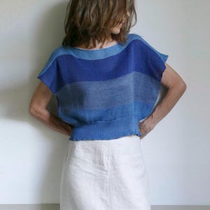 Könnte beinhalten: Ein kurzärmeliges Strickoberteil mit horizontalen Streifen in Blau- und Grautönen und einem breiten gerippten Saum, kombiniert mit einem knielangen cremeweißen Rock und hellgrauen Turnschuhen mit weißen Schnürsenkeln und dicken Sohlen.
