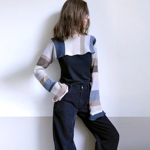 May include: A person wearing a striped long-sleeved shirt with a black top underneath and dark blue wide-leg jeans. They are wearing blue sneakers.