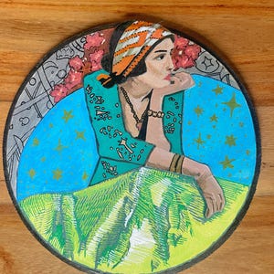 May include: Circular painting depicting a woman in a teal jacket and orange headscarf, resting her chin on her hand. The background features a blue sky with gold stars, pink flowers, and a green landscape.