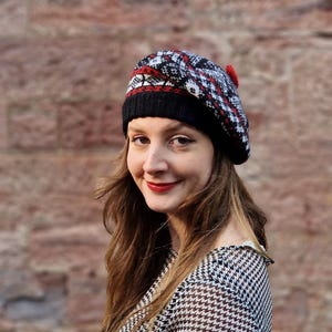 Puede incluir: Boina estampada en negro, rojo y blanco, con un pequeño pompón rojo. La boina se lleva con una parte superior con estampado de pata de gallo en blanco y negro. El fondo es una pared de ladrillo texturizada.
