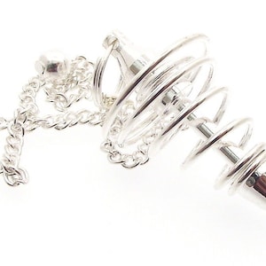 May include: A silver pendulum with a spiral design and a pointed tip. The pendulum is suspended from a chain and a small ball. The design is intricate and detailed, with a polished finish.