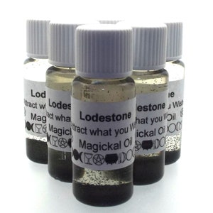 Puede incluir: Seis pequeñas botellas de vidrio con tapas y etiquetas blancas. Las etiquetas son blancas con texto negro que dice "Lodestone Attract what you Wish Magickal Oil".