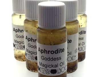 May include: Six small glass bottles with white lids filled with a clear liquid and brown flakes. The bottles have labels that say "Aphrodite Goddess Magickal Oil" with symbols and text.