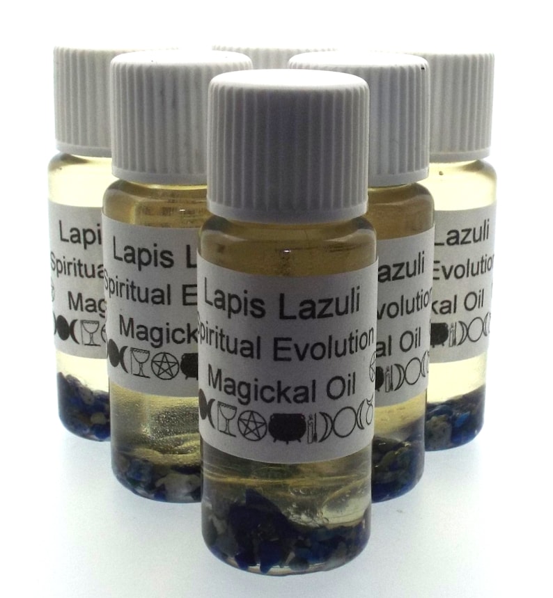 May include: Six small glass bottles with white lids filled with a clear liquid and blue crystals. The bottles have white labels with the text "Lapis Lazuli Spiritual Evolution Magickal Oil" printed on them.
