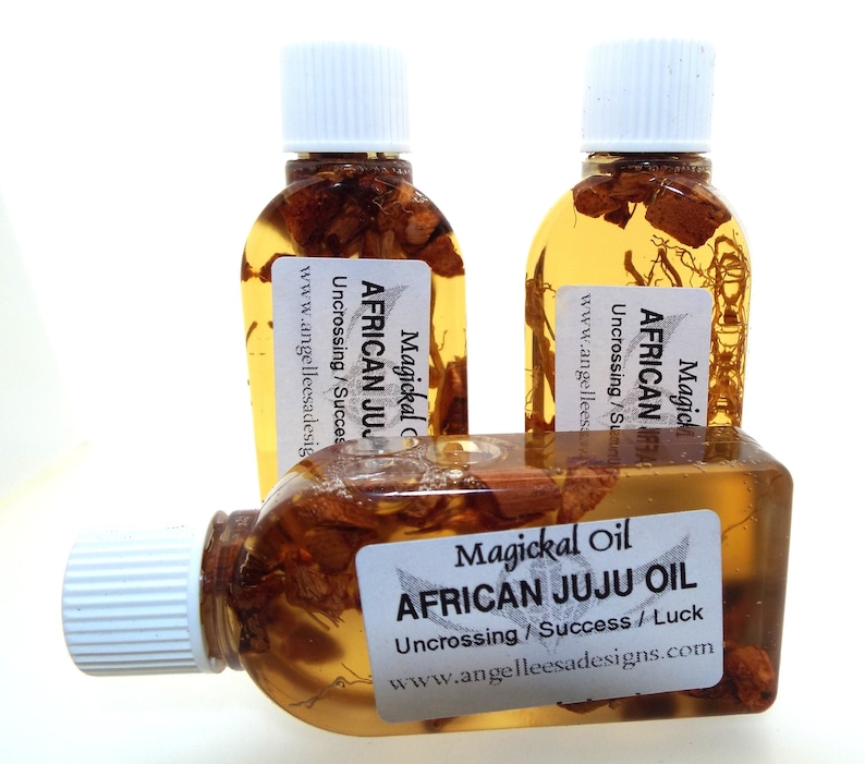 May include: Three small glass bottles filled with a golden liquid and herbs. The bottles have white labels with the text "Magickal Oil African Juju Oil Uncrossing/Success/Luck www.angelleesadesigns.com".