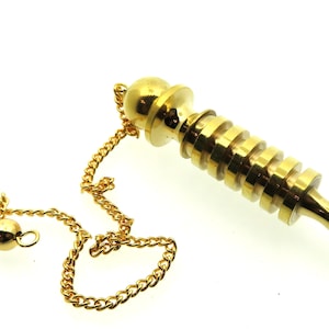 Könnte beinhalten: Ein goldfarbenes Metallpendel mit einer spitzen Spitze und einer Kette. Das Pendel hat eine Reihe von Ringen um den Körper.