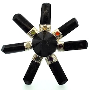 Peut inclure: Un générateur d'énergie orgone noir avec un cristal noir central et sept baguettes de tourmaline noire rayonnant vers l'extérieur. Chaque baguette est ornée d'une bande argentée et d'une petite pierre précieuse colorée. Le design est symétrique et géométrique.