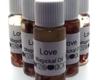 May include: Six small glass bottles with white lids filled with a clear liquid and small pieces of dried flowers. Each bottle has a white label with the text "Love Magickal Oil" printed in black.
