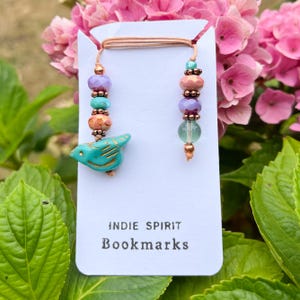 May include: Two handmade beaded bookmarks. One has a turquoise bird charm, the other has colourful beads. The bookmarks are attached to a white card with the text "INDIE SPIRIT Bookmarks".
