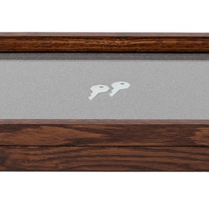 May include: A rectangular wooden display case with a glass top and brass-colored latches. The interior features a gray fabric lining and two small white keys. The wood has a dark brown finish.