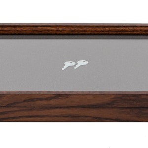 May include: A rectangular wooden display case with a glass top and brass-colored latches. Inside, two small, white keys rest on a gray fabric surface. The wood has a dark brown finish.