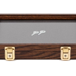 May include: A rectangular wooden display case with a glass top and two keys inside. The case is made of dark brown wood with brass-colored latches. The interior has a gray fabric lining.