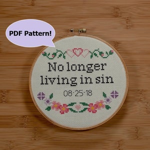 May include: A white embroidery hoop with a cross-stitch design that reads "No longer living in sin" with the date "08-25-18" below. The hoop is surrounded by a floral border with pink and purple flowers.