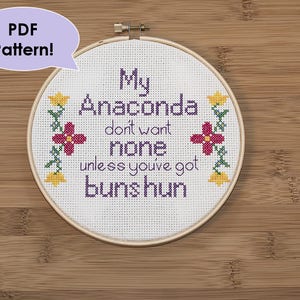Peut inclure: Un cerceau de broderie blanc avec un motif de point de croix qui dit "My Anaconda don't want none unless you've got buns hun". Le motif est entouré de petites fleurs jaunes et violettes.