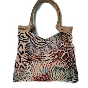 Op de afbeelding: Een tote bag met een geweven dierenprint. De tas heeft een mix van zebra-, slang- en luipaardpatronen in beige, bruin en zwart. Hij heeft een beige handvat en een rechthoekige vorm.