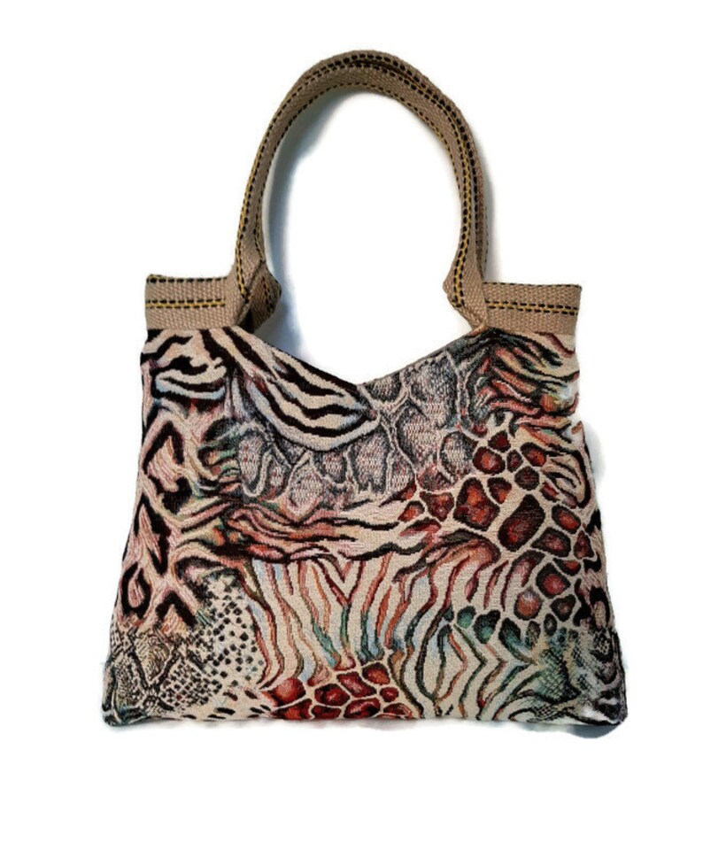 Op de afbeelding: Een tote bag met een geweven dierenprint. De tas heeft een mix van zebra-, slang- en luipaardpatronen in beige, bruin en zwart. Hij heeft een beige handvat en een rechthoekige vorm.