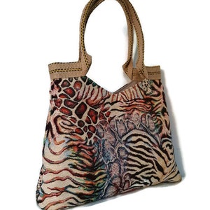 Op de afbeelding: Een tote bag met een levendig dierenprintontwerp. De tas heeft een mix van patronen, waaronder luipaardvlekken, zebra strepen en een slangenhuidachtige textuur. Het heeft stevige bruine handvatten en een bijpassende afwerking.
