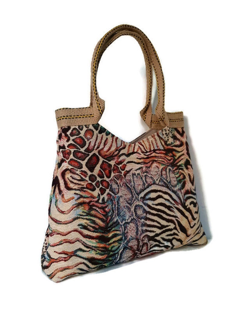 Op de afbeelding: Een tote bag met een levendig dierenprintontwerp. De tas heeft een mix van patronen, waaronder luipaardvlekken, zebra strepen en een slangenhuidachtige textuur. Het heeft stevige bruine handvatten en een bijpassende afwerking.