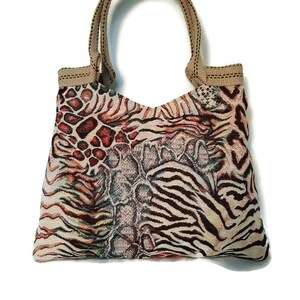 Op de afbeelding: Een tote bag met een uniek dierenprint ontwerp. De tas heeft een combinatie van patronen, waaronder zebra strepen, luipaardvlekken en een slangenleer textuur. Het heeft een beige handvat en afwerking, tegen een witte achtergrond.