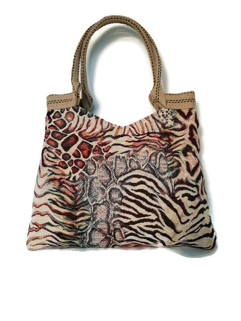 Op de afbeelding: Een tote bag met een uniek dierenprint ontwerp. De tas heeft een combinatie van patronen, waaronder zebra strepen, luipaardvlekken en een slangenleer textuur. Het heeft een beige handvat en afwerking, tegen een witte achtergrond.