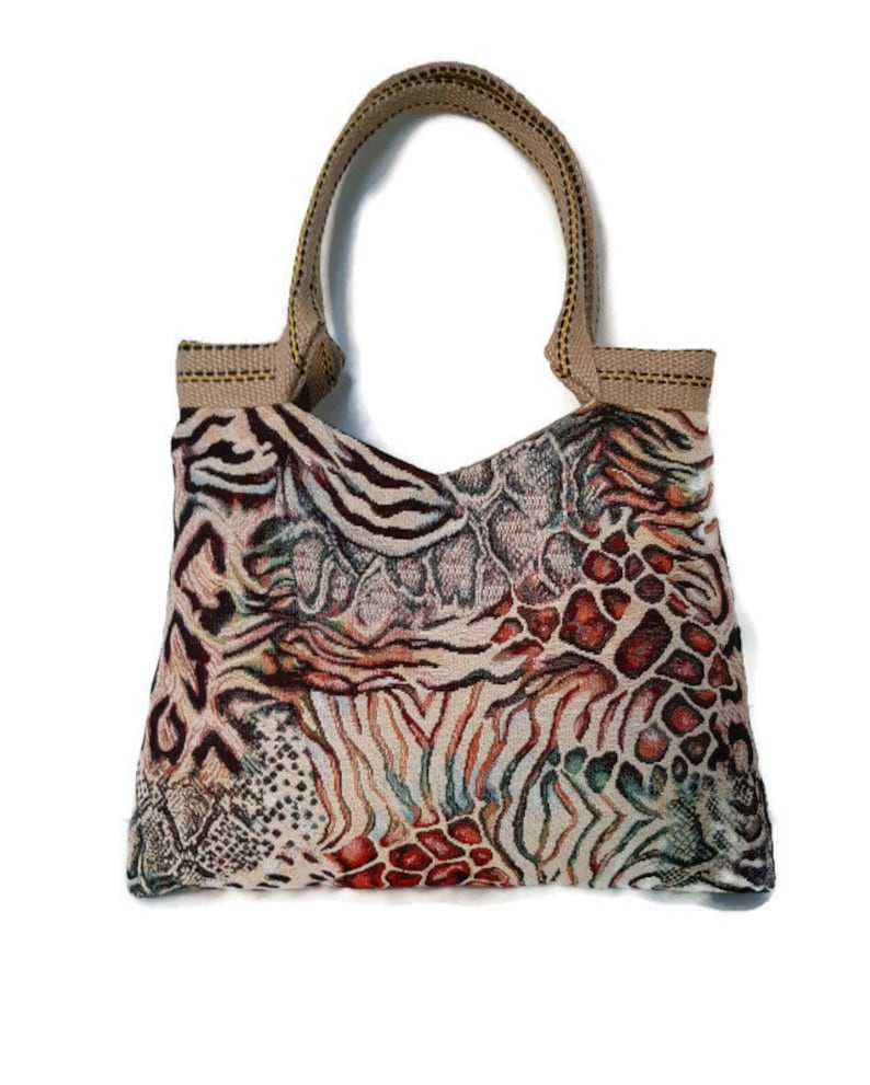 Op de afbeelding: Een tote bag met een uniek dierenprint ontwerp. De tas heeft een mix van zebra strepen, reptielschubben en luipaardvlekken in bruin, beige, rood en groen. De handvatten zijn bruin.