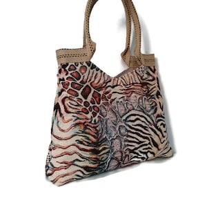 Op de afbeelding: Een patroon draagtas met een beige handvat en een mix van dierenprints. De tas heeft een combinatie van luipaard-, zebra- en slangenleerpatronen in tinten bruin, beige en zwart. De tas is gemaakt van een geweven stof.