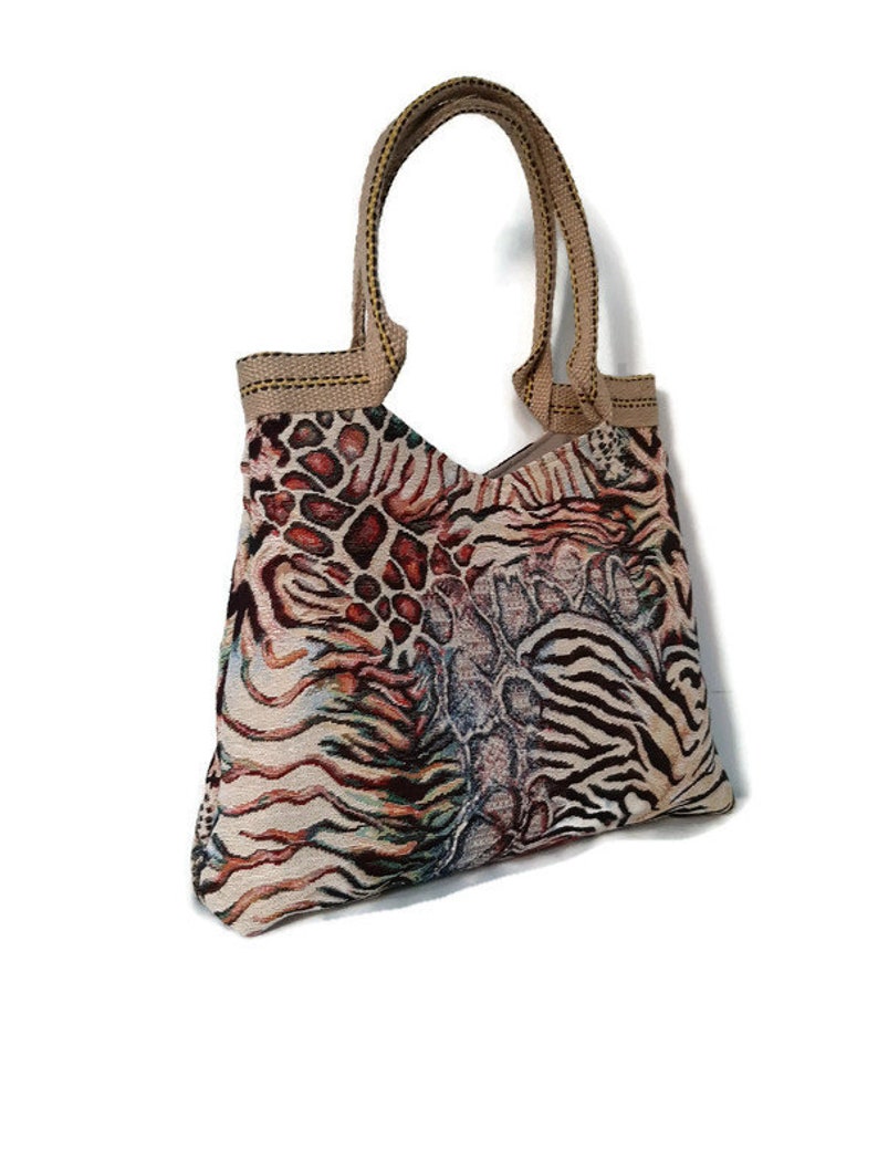 Op de afbeelding: Een patroon draagtas met een beige handvat en een mix van dierenprints. De tas heeft een combinatie van luipaard-, zebra- en slangenleerpatronen in tinten bruin, beige en zwart. De tas is gemaakt van een geweven stof.