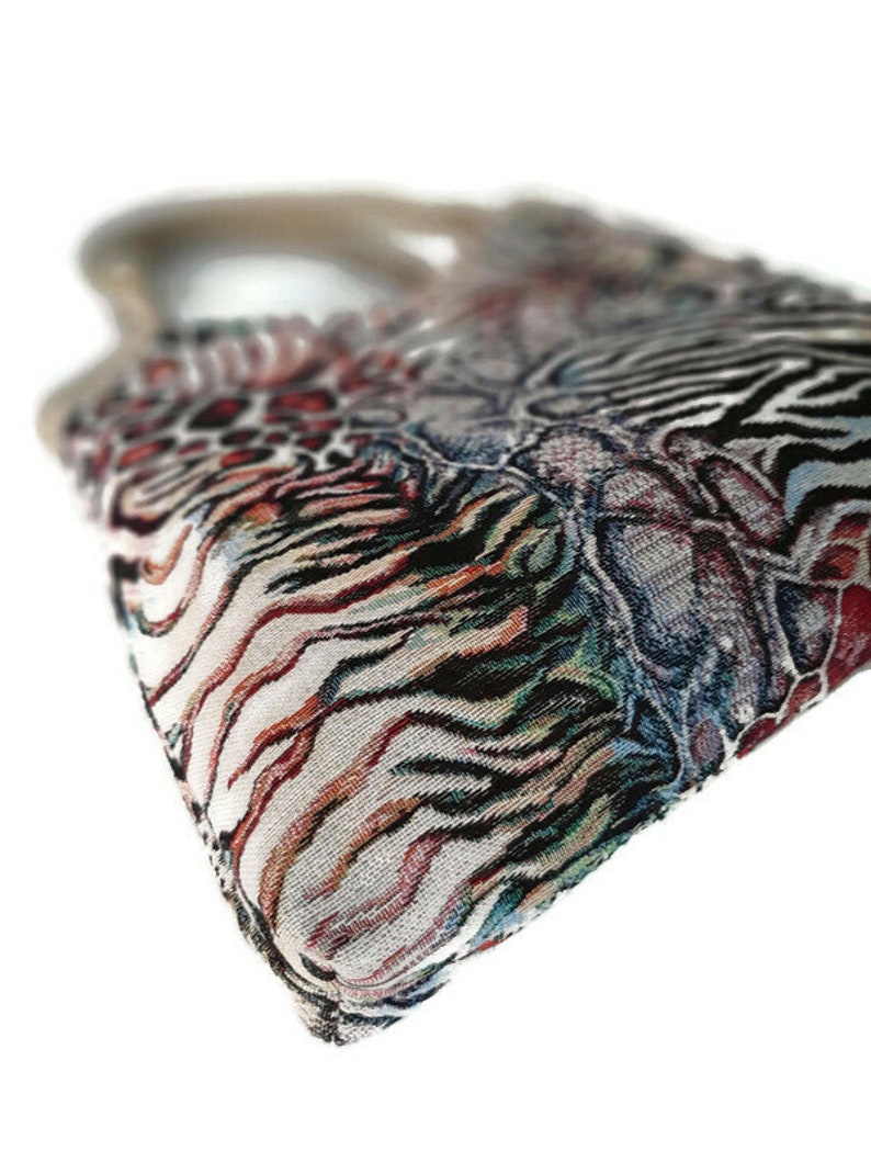 Op de afbeelding: Een handtas met patroon en een geweven ontwerp. De tas heeft een mix van dierenprints, waaronder zebra strepen en luipaardvlekken, in tinten zwart, bruin, rood en wit. De handgreep is lichtbruin.