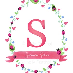 May include: Pink letter S surrounded by a wreath of green vines, pink hearts, and ladybugs with black spots. The wreath is on a white background. A pink ribbon with the text "Sannie Jean" is below the letter.