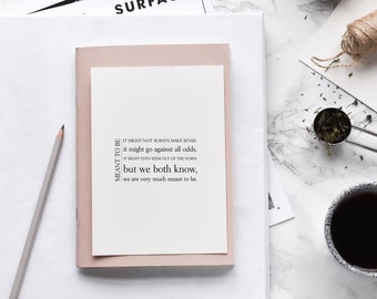 May include: A pink notebook with a white page inside. The page has a quote about being meant to be, written in black text. The quote reads: "It might not always make sense. It might go against all odds. It might even seem out of the norm. But we both know, we are very much meant to be."