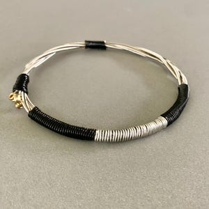 May include: A black and silver guitar string bracelet. The bracelet is made of multiple guitar strings that have been woven together and then wrapped with black and silver wire.