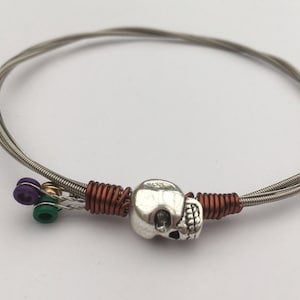 Pulsera de cuerdas de guitarra recicladas, con una cuenta de calavera y alambre de cobre. Regalo único unisex para guitarristas.