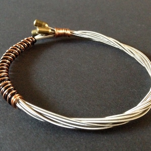May include: A bracelet made from repurposed guitar strings. The bracelet is silver and copper in colour and has a coiled section.