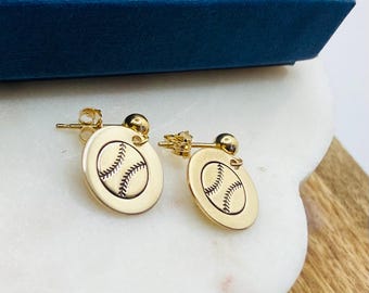 May include: A pair of gold earrings with a baseball design. The earrings are round and have a textured surface.