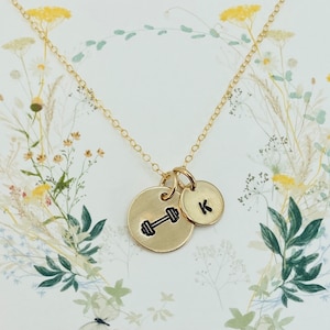 May include: Gold necklace with two charms. One charm is a dumbbell and the other charm is a letter K.