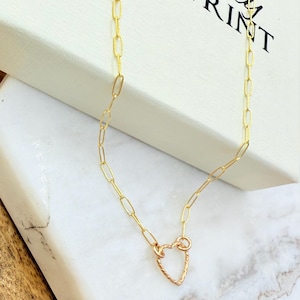 May include: A gold-colored chain necklace with a heart-shaped pendant. The necklace has a delicate, elongated link chain. The heart pendant has a textured surface. The necklace is displayed on a white box with the text "Uniquely Imprint".