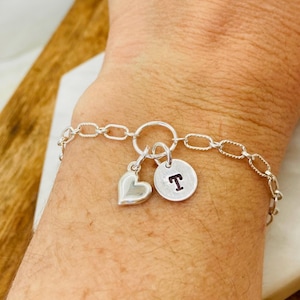 May include: Silver charm bracelet with a heart charm and a round charm with the letter "T". The bracelet has a chain link design.